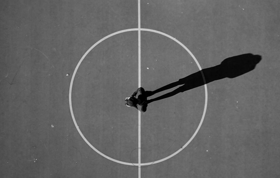 Man standing on a soccer field, viewed from the above, his shadow breaks the lines on the ground